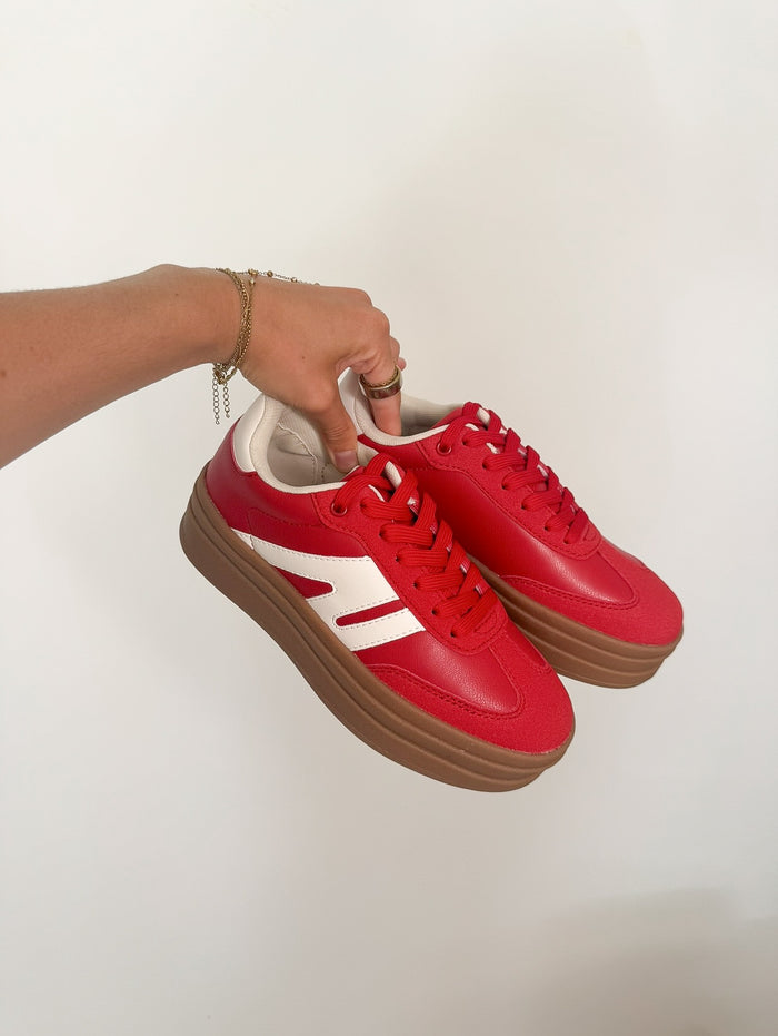 Red sneakers with white accents held by a hand on a light background