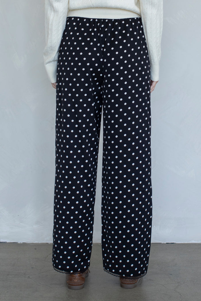 Black pants with white polka dots worn by a person against a plain background