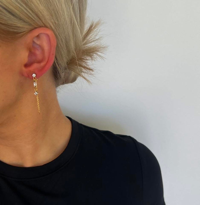 Close-up of a person wearing gold earrings with a plain background