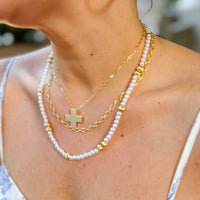 Close-up of a person wearing a gold chain and pearl necklace with a cross pendant.