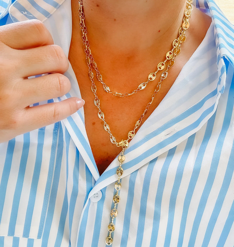 Gold chain necklace worn by a person in a blue and white striped shirt.