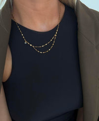 Gold chain necklace worn by a person against a neutral background
