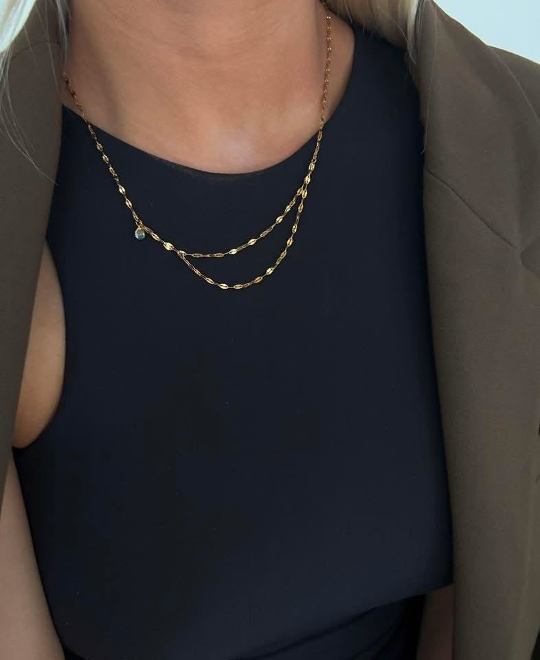 Gold chain necklace worn by a person against a neutral background