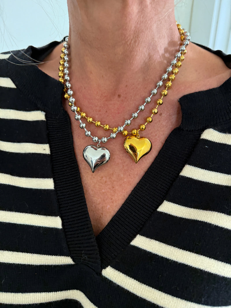 Person wearing a necklace with heart-shaped pendants in front of a striped shirt.